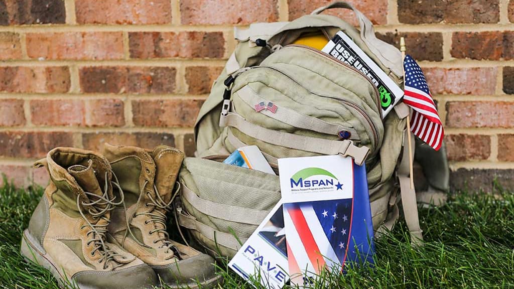 A pair of boots sits aside a backpack displaying the USA flags and flyers for MVC programs.